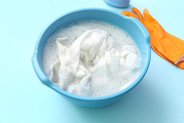 Plastic basin with dirty clothes, water, foam and orange rubber gloves on blue background