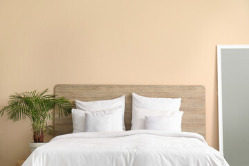 Comfortable bed with white pillows, mirror and houseplant in bedroom - obrazy, fototapety, plakaty