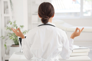 Female doctor meditating in clinic, back view - obrazy, fototapety, plakaty