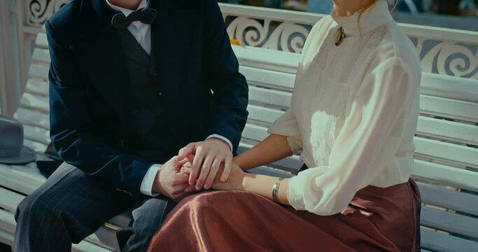 romantic date in 19th century, man and woman holding hands and sitting on bench in park, 4K, Prores