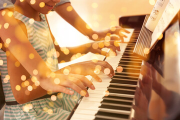 Christmas and New Year music. Woman with little girl to play piano indoors. Bokeh effect