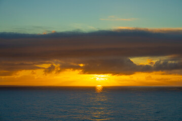 Fototapeta na wymiar A Coastal Canvas Unfurls as Clouds Soften the Sun's Fiery Goodbye over the Ocean Horizon