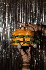 Vertical photo. Female hand in black tulle glove with polka dot pattern holds juicy tasty burger...