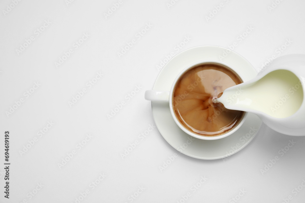 Poster Pouring milk into cup of coffee on white background, top view