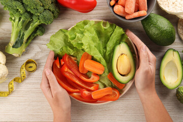 Healthy diet. Woman with fresh vegetables and measuring tape at light wooden table, top view