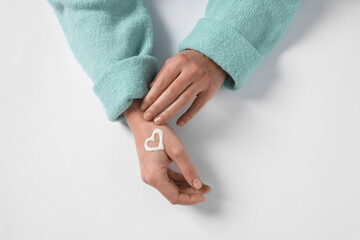 Woman with heart made of cosmetic cream on hand against white background, top view