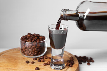 Pouring coffee liqueur from bottle into glass and beans at light table