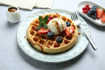 Delicious Belgian waffles with ice cream, berries and caramel sauce served on grey table, closeup
