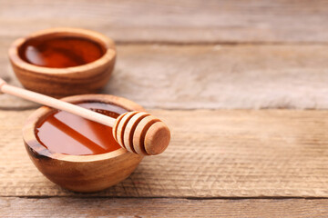 Delicious honey in bowls and dipper on wooden table. Space for text