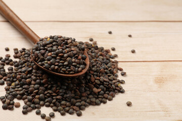 Spoon and many raw lentils on light wooden table, closeup. Space for text