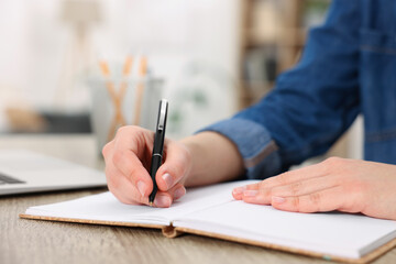Young woman writing in notebook at wooden table, closeup