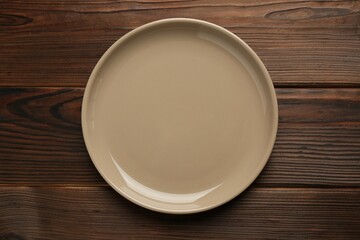 Beautiful beige ceramic plate on wooden table, top view