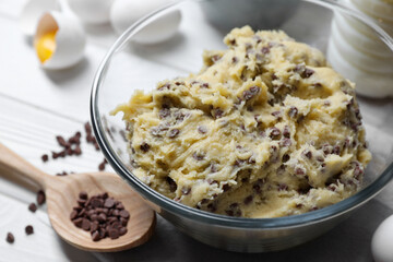 Chocolate chip cookie dough in bowl and ingredients on white wooden table, closeup