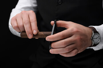 Man cutting tip of cigar on black background, closeup