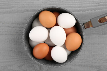 Unpeeled boiled eggs in saucepan on grey wooden table, top view