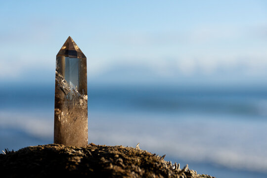 A close up image of a healing smoky quartz crystal tower with the blue Pacific Ocean in the background. 
