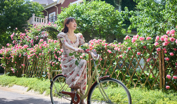 Young and beautiful women ride bicycles in the courtyard full of flowers