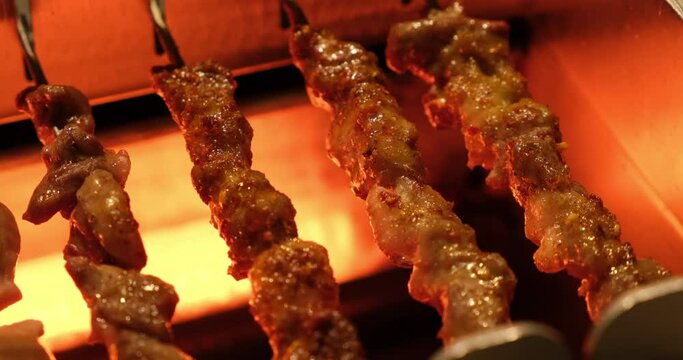 close up several lamb skewers rotating on automatic barbecue grill