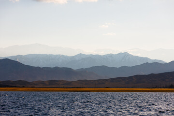 Blue calm water in Issyk-Kul lake with mountains on background at autumn afternoon.