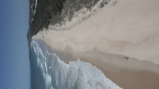 Vertical format low flight along endless sandy beach in NSW, Australia