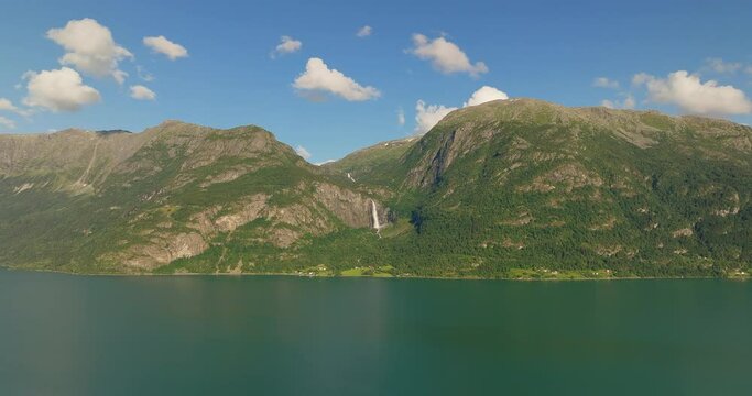 Aerial establishing overview of waterfall cascading in distance of Lustra Fjorden Fjord Norway in the summer
