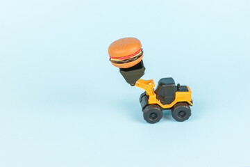 A bulldozer carrying a hamburger on a blue background. © kvladimirv