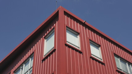 Rectangular windows on red corrugated facade against blue sky, facade corner