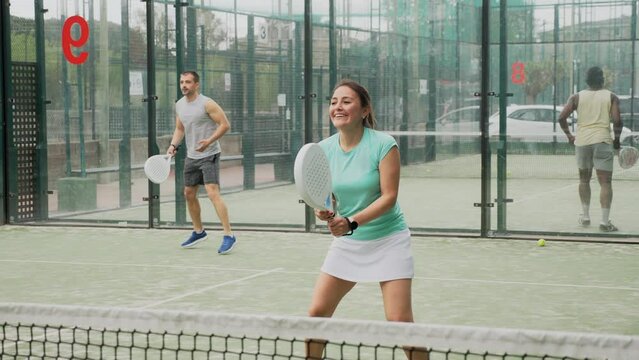 Young adult woman playing paddle tennis with friends at warm sunny day