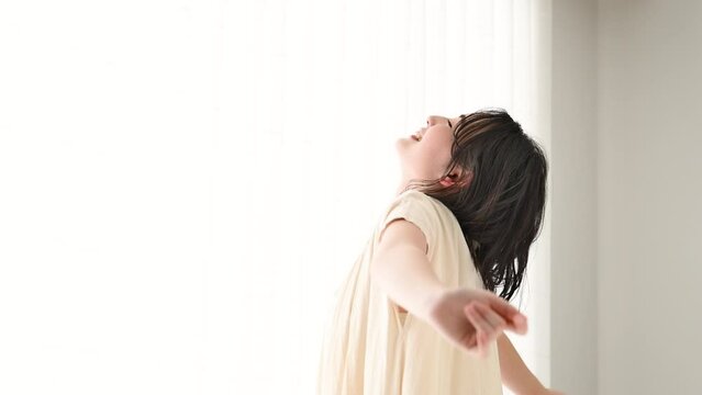 窓辺に佇む若い女性　笑顔で深呼吸をする動画