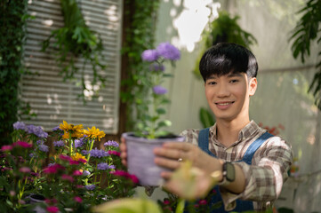 Young positive Asian male florist is working at plant nursery and taking care of the potted flowers.