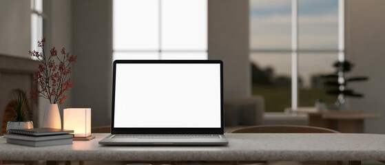Front view of a white-screen laptop computer and accessories on a table in a cosy home.