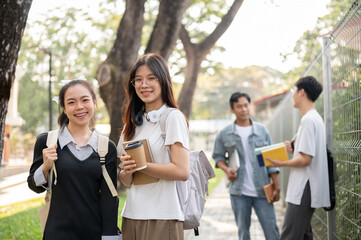 Two charming Asian female students with their backpack are standing on a footpath on their campus.