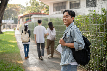 Positive Asian male student with backpack is walking to school, walking on a footpath on his campus.
