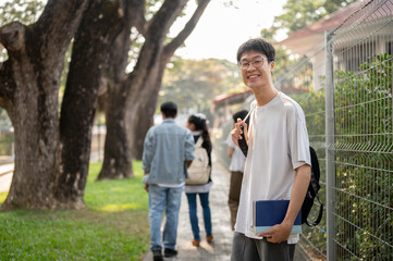 Positive Asian male student with backpack is walking to school, walking on a footpath on his campus.