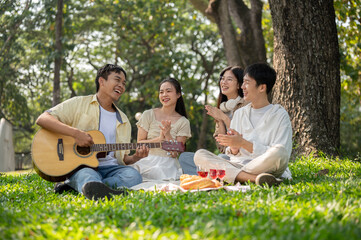 Group of cheerful Asian friends are enjoying a picnic in a park together, singing and playing guitar