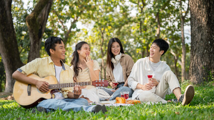 A group of happy young Asian friends is enjoying a picnic in a green park on a summer day together.