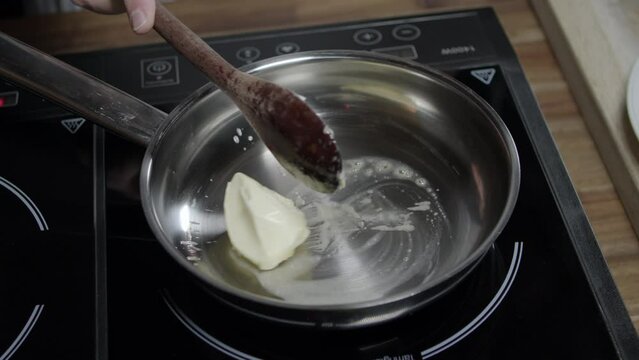 Chef adds butter with a spoon in hot pan to prepare cafe de paris butter sauce, on induction stove