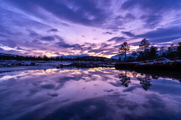 Arktyczny krajobraz odbijający się na powierzchni wody, w fioletowych barwach zachodzącego słońca