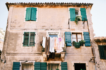Fototapeta na wymiar Colorful laundry dries on lines on the balcony of an ancient stone house with green wooden shutters