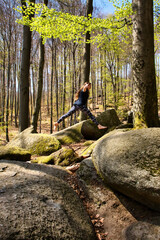 Teenage girl leaping from one rock to another on a spring day at Felsenmeer in Germany. - obrazy, fototapety, plakaty