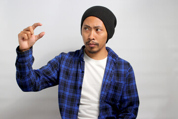 A displeased Asian man, dressed casually in a beanie hat and casual clothes, is gesturing a small...