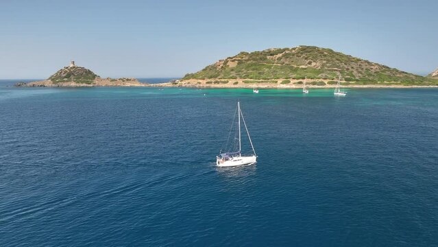 Sailing boat cruising over the calm blue sea in front of the coast of Corsica. Drone panning shot
