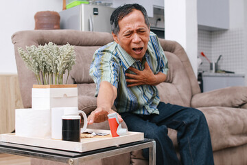 Old man suffering from asthma attack, having trouble breathing while reaching for inhaler while sitting on the sofa - obrazy, fototapety, plakaty