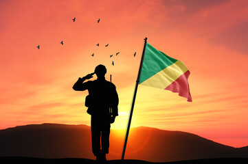 Silhouette of a soldier with the Congo flag stands against the background of a sunset or sunrise....
