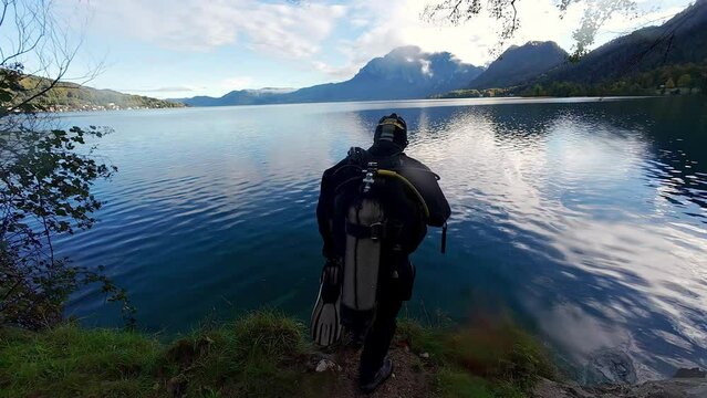 A diver gets ready and jumps into a beautiful lake with mountains in the background.