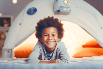 Joyful afro american child lying on his stomach inside a cozy blanket-forte resembling a space theme, with stars and a rocket ship, suggesting playful adventure and wonders of child's imagination - obrazy, fototapety, plakaty
