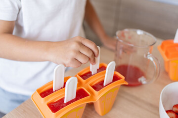 The process of making ice cream. Child making tasty ice lollipops in moulds on countertop in kitchen during free time.