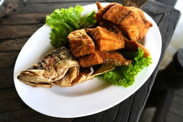 Fried slide salt fish in Thai style with vegetables decoration on white plate serve on woden table in Thai restaurant.