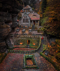 Hresko, Czech Republic - Aerial view of a lovely stone cottage in the Czech woods near Hresko at autumn with colorful fall foliage and man in red jacket and hoodie walking up the stairs