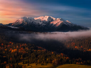 Slovakia - Aerial autumn view of the peaks of the High Tatras mountains in national park at sunrise with colorful autumn foliage, fog and dramatic golden sky